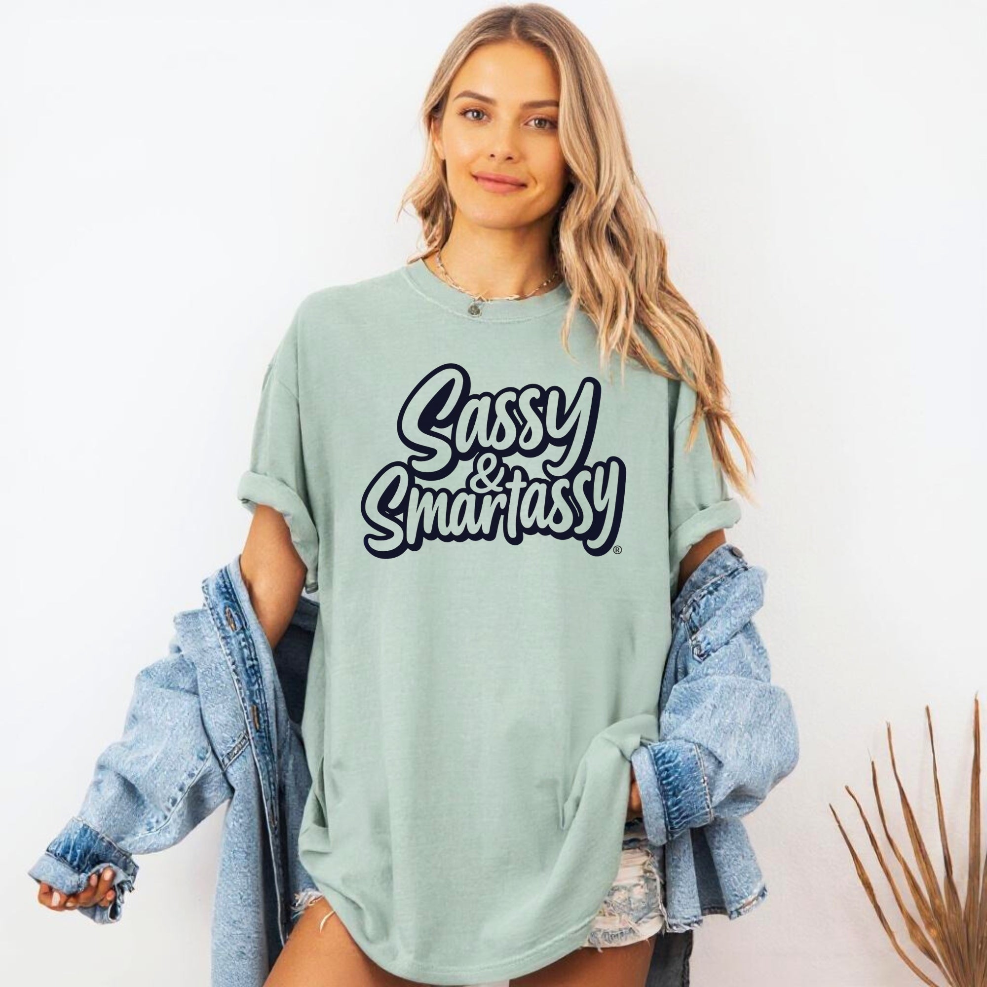 Woman wearing a light green oversized t-shirt with 'Sassy & Smartassy' text, holding a denim jacket.