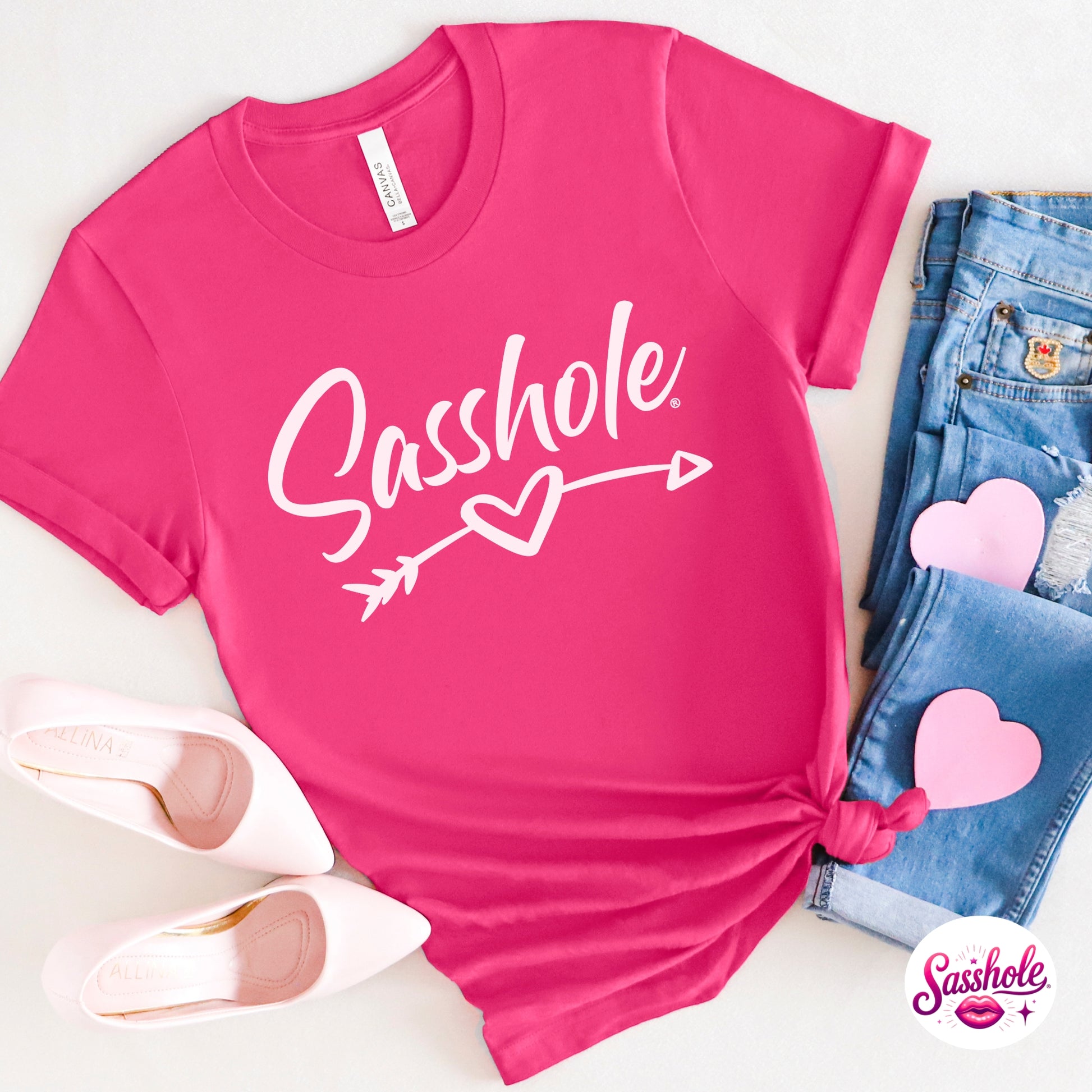 Pink t-shirt with 'Sashole' text and heart design, paired with jeans and shoes on a white background.
