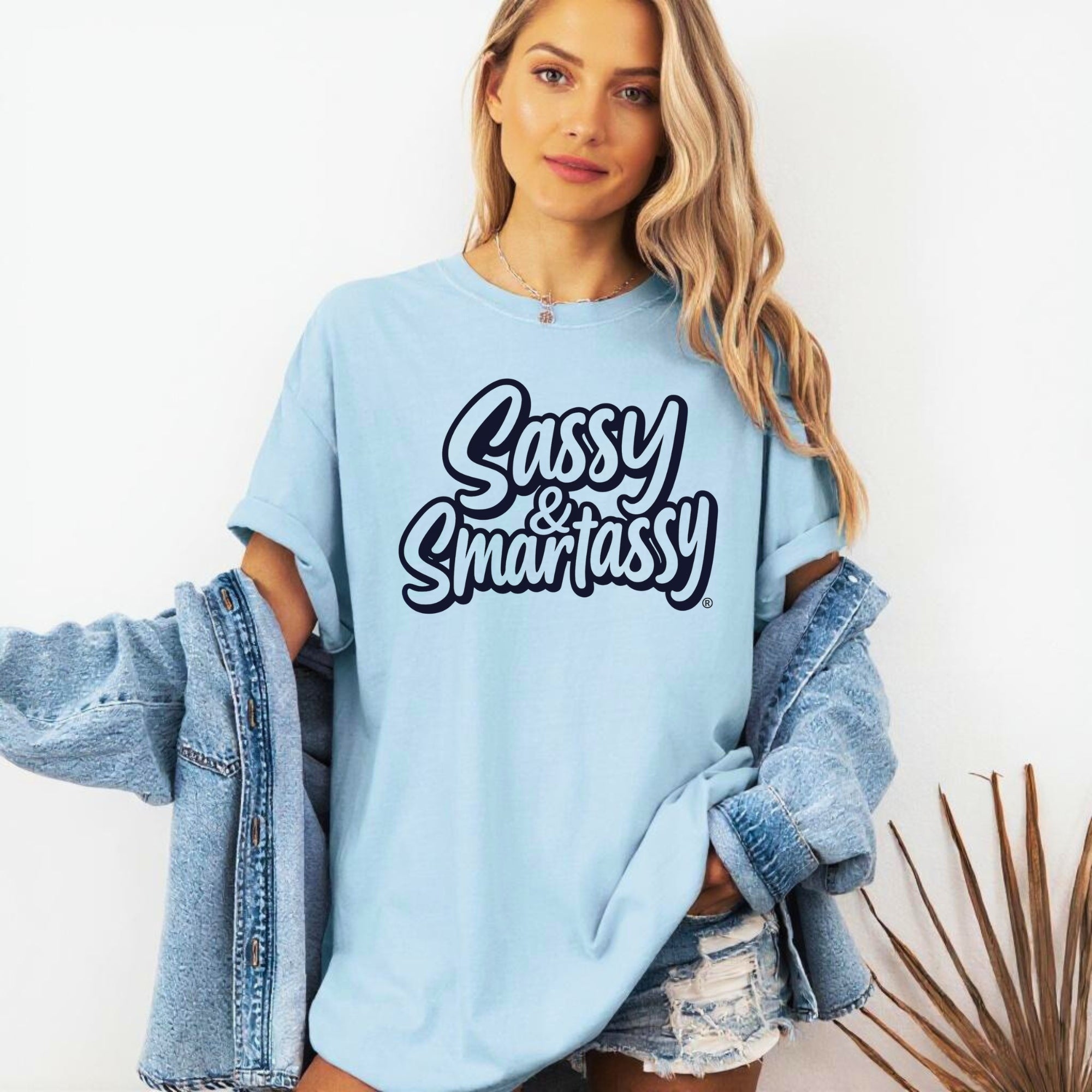 Woman wearing a light blue sweatshirt with 'Sassy & Smartassy' text, holding a denim jacket.
