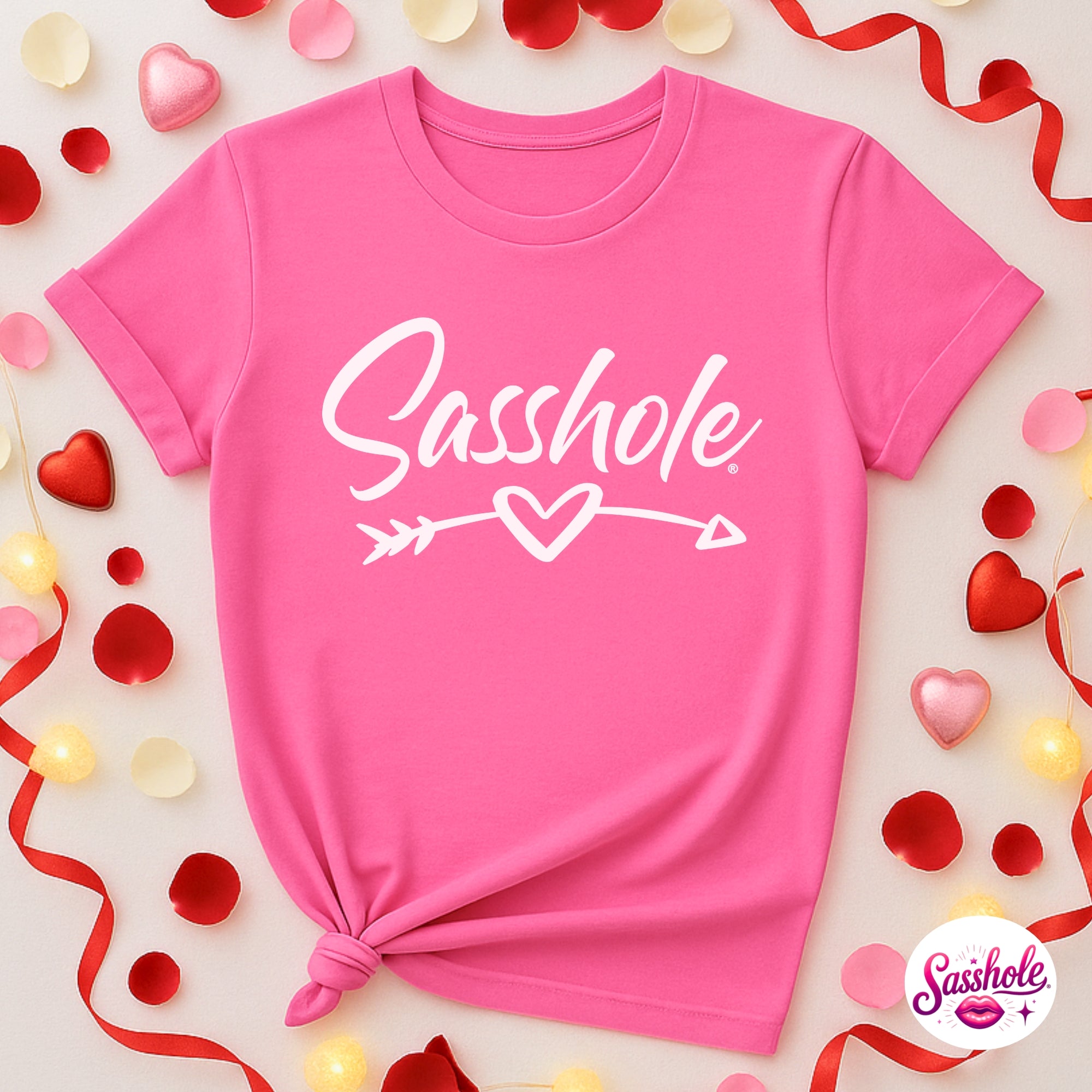 Image of Pink t-shirt with 'Sasshole' text surrounded by decorative elements on a light background