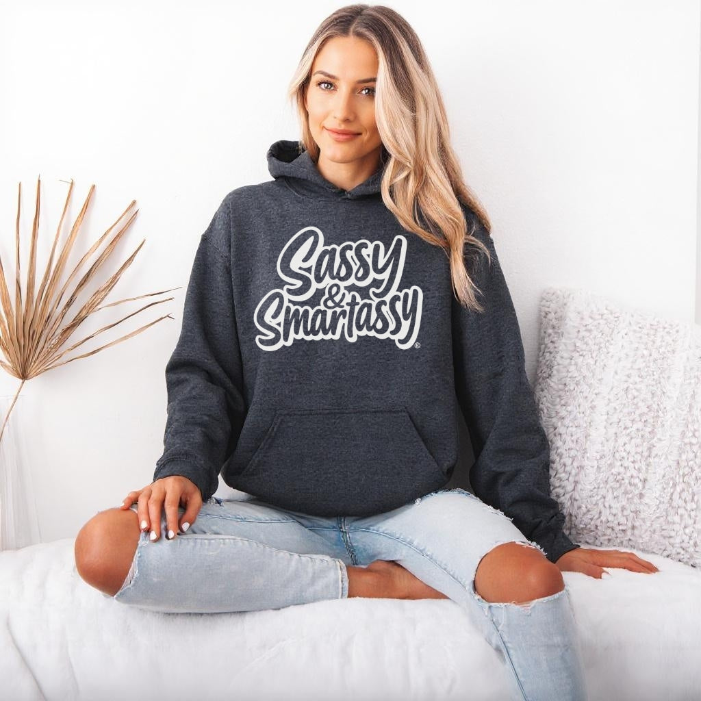 Woman wearing a dark gray hoodie with 'Sassy & Smartassy' text, sitting on a white couch.