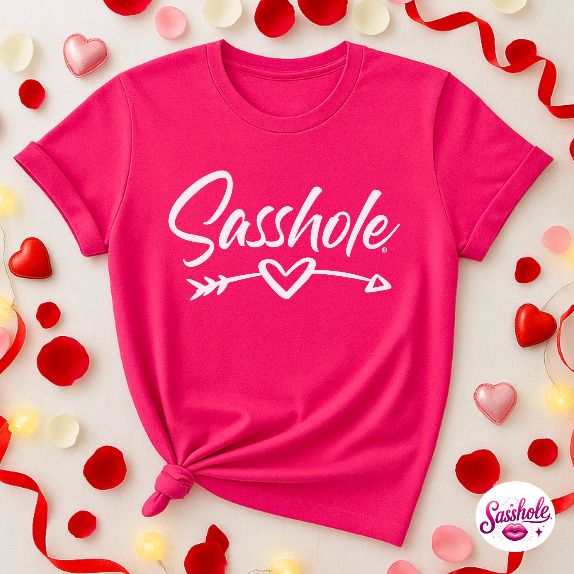 Image of Pink t-shirt with 'Sasshole' text and heart design on a decorative background with hearts and ribbons.