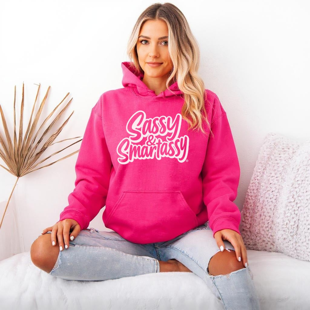 Woman wearing a hot pink hoodie with 'Sassy & Smartassy' text, sitting on a white couch.