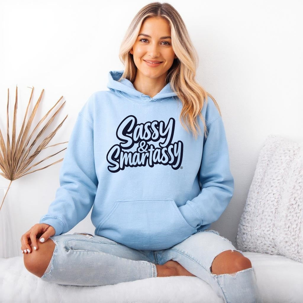 Image of Woman wearing a light blue hoodie with 'Sassy & Smartassy' text, sitting on a white couch.