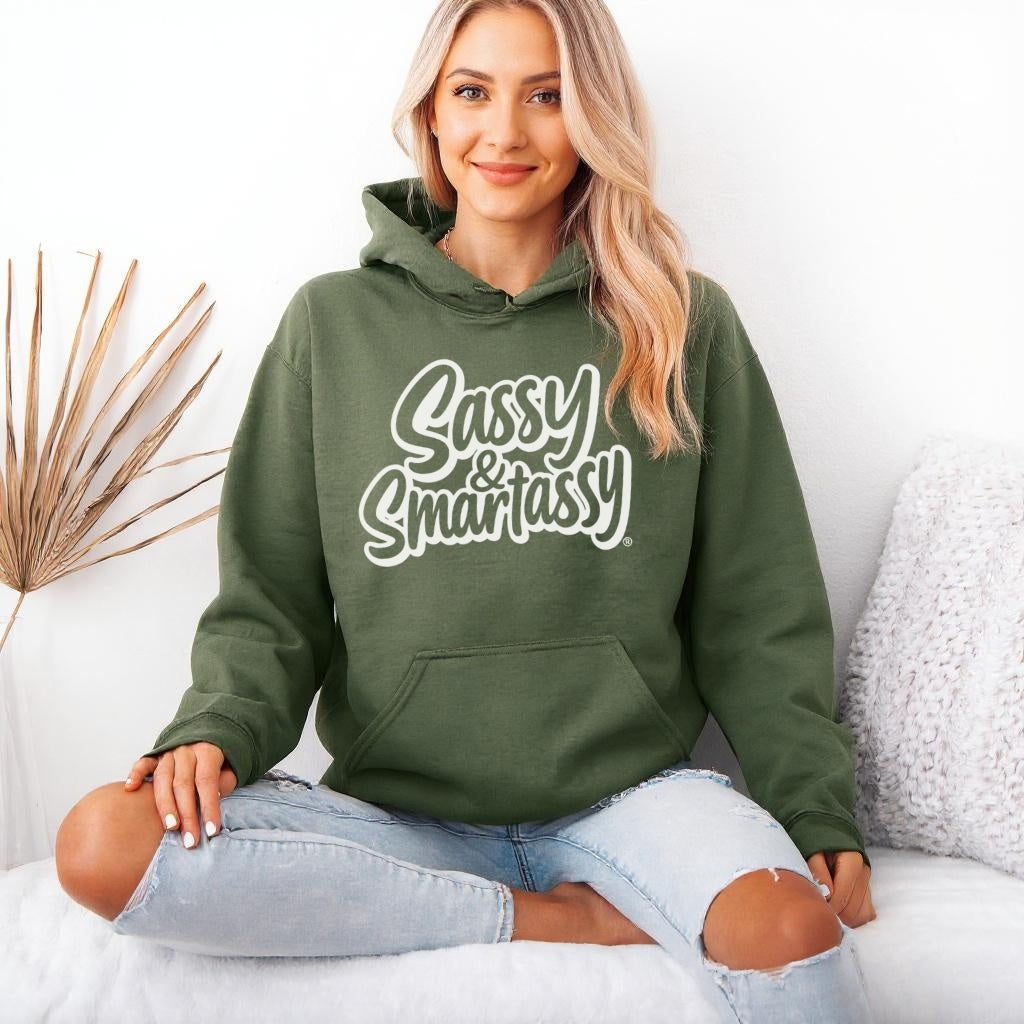 Woman wearing a military green hoodie with 'Sassy & Smartassy' text, sitting on a white couch.
