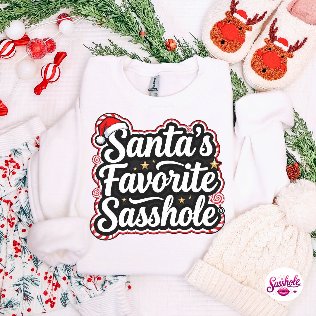 White sweatshirt with 'Santa's Favorite Sasshole' text on a festive background with cookies and greenery.