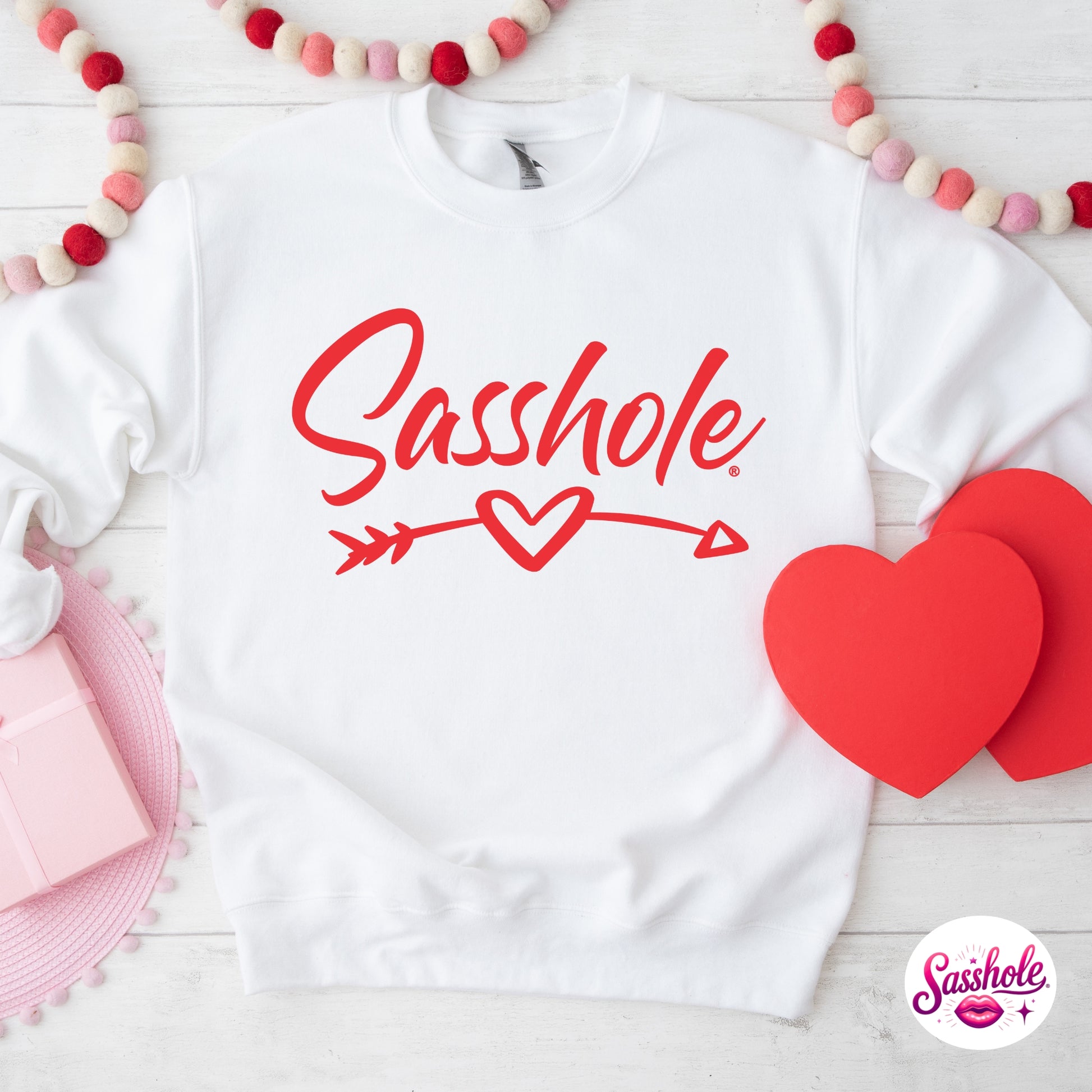 White sweatshirt with 'Sasshole' text and red hearts on a white background