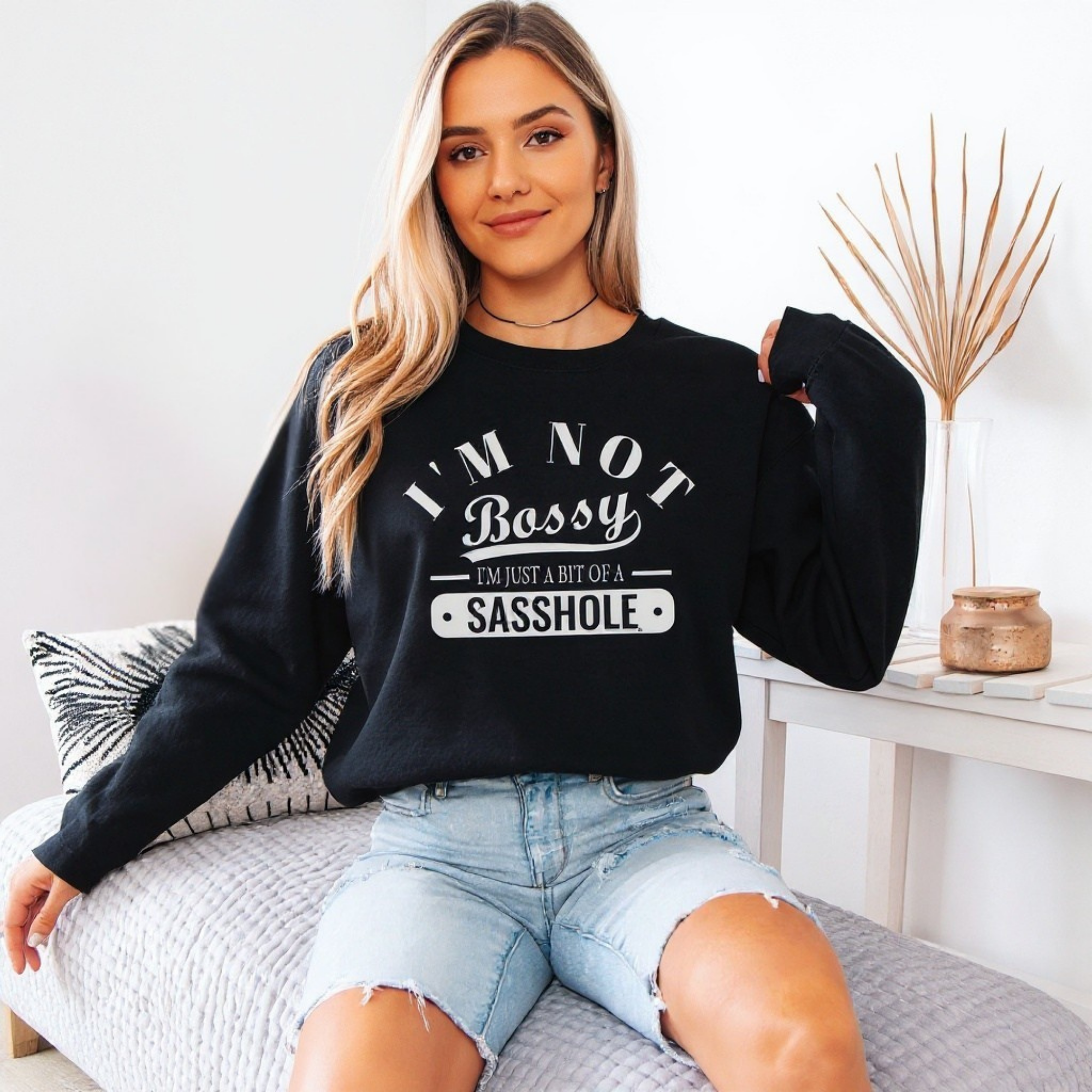 Woman wearing a black sweatshirt with text, sitting on a couch in a room.