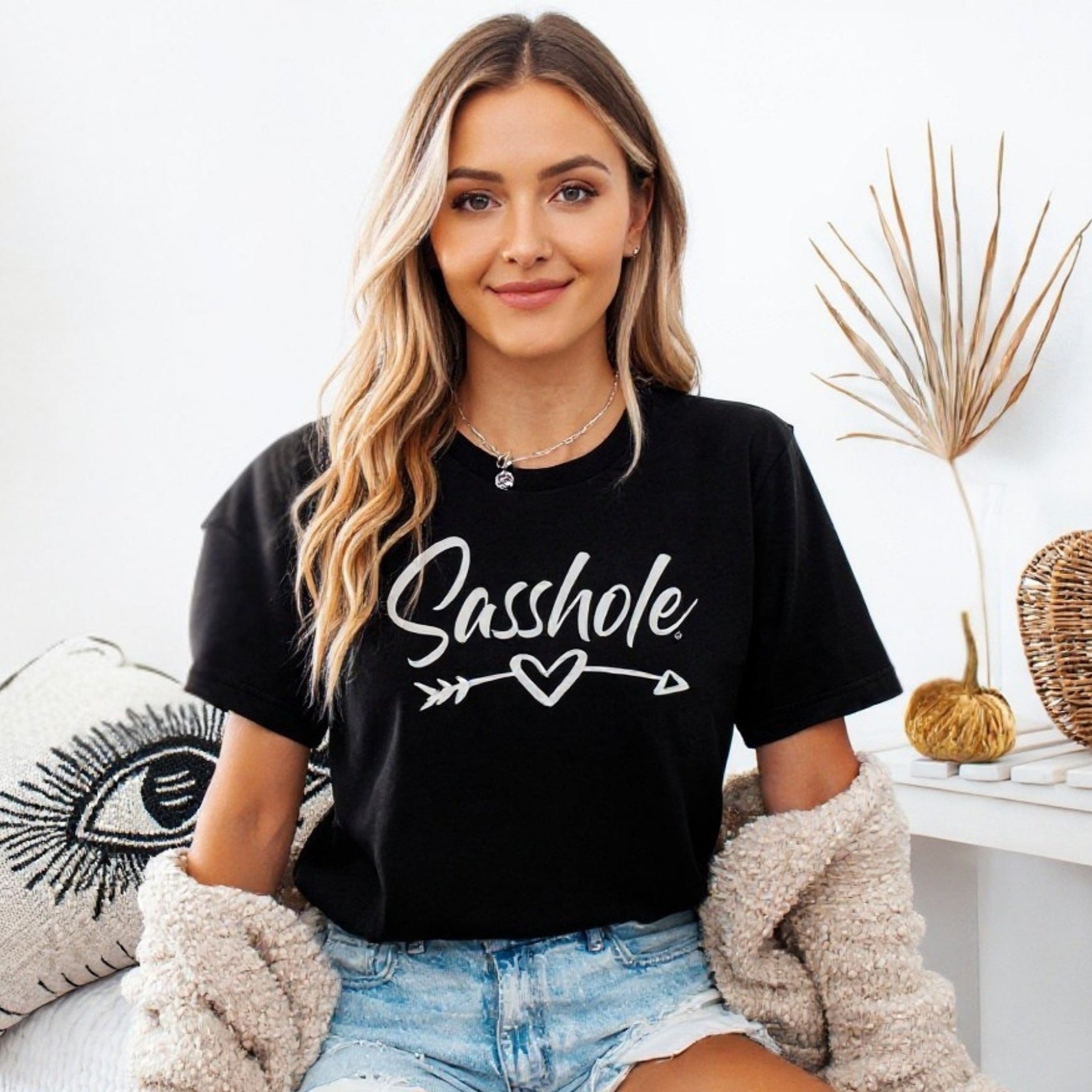 Image of Woman wearing a black t-shirt with 'Sasshole' text, sitting on a couch.