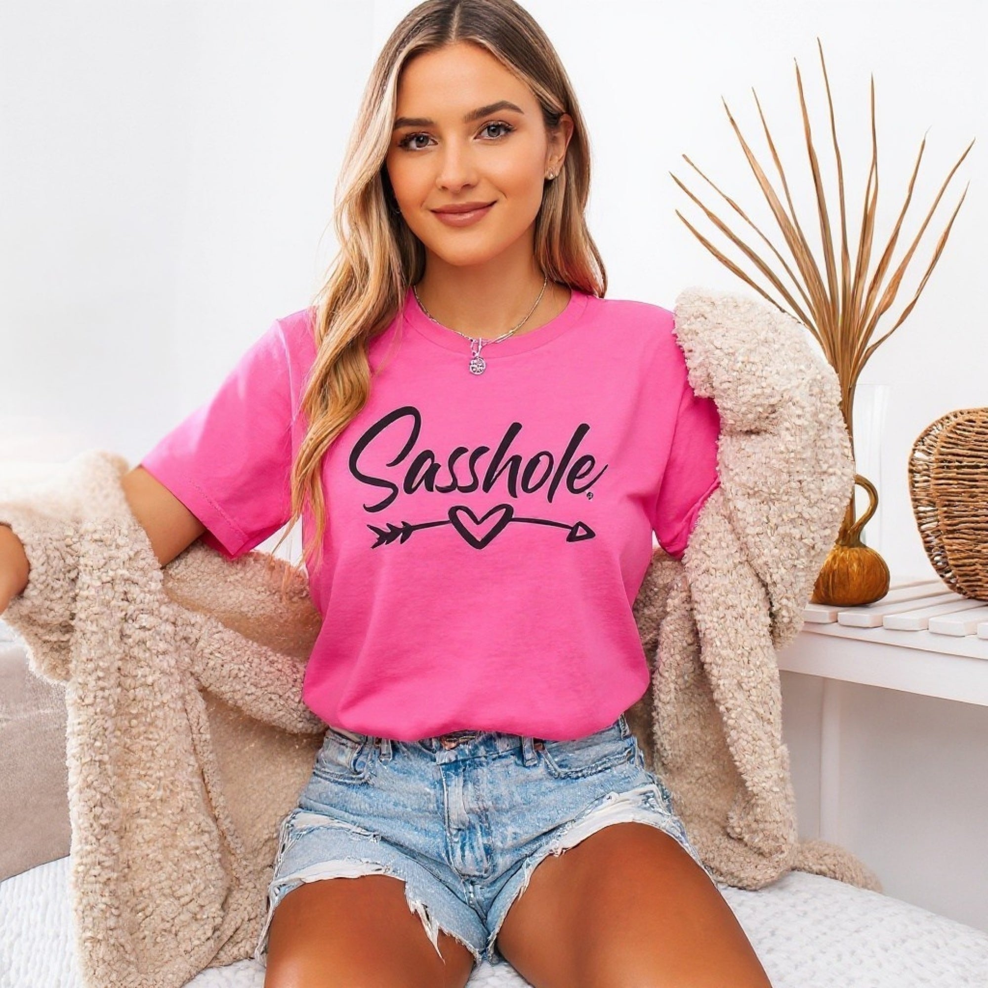 Woman wearing a pink t-shirt with 'Sasshole' text, sitting on a couch.