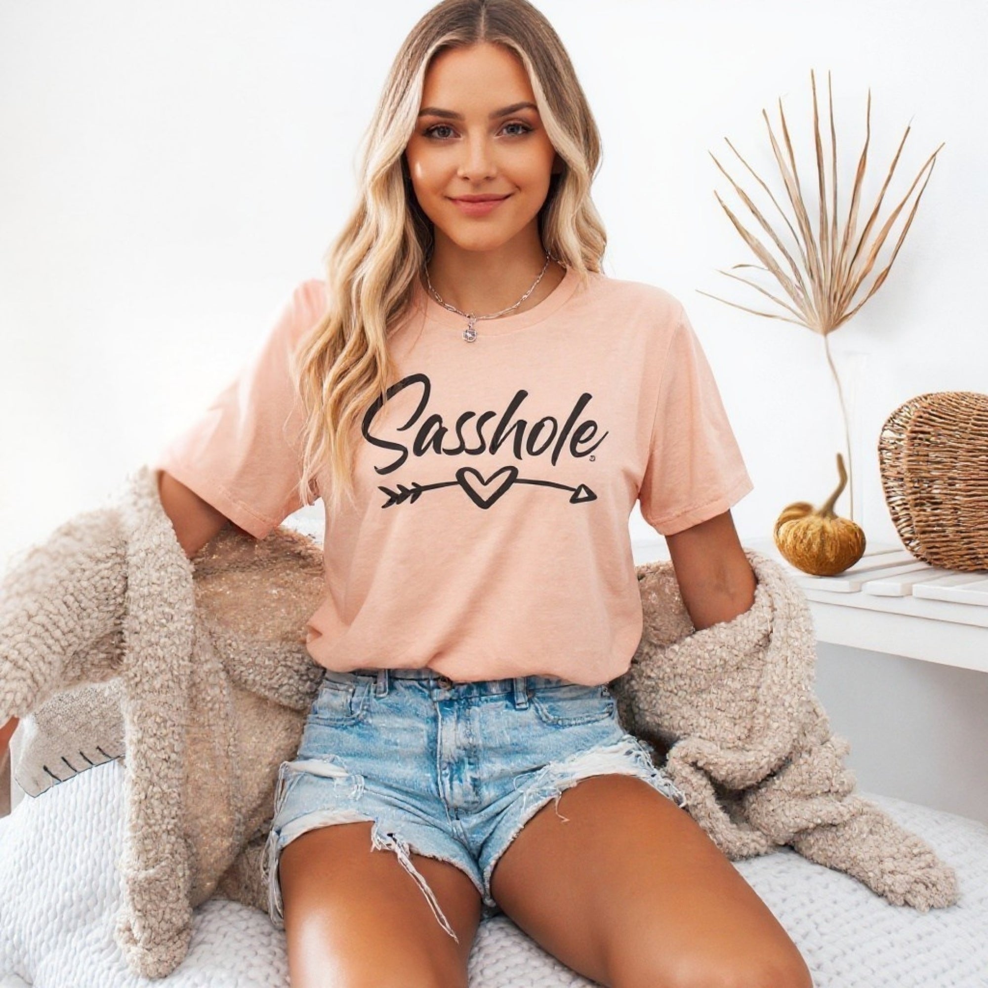 Image of Woman wearing a pink t-shirt with 'Sasshole' text, sitting on a couch.